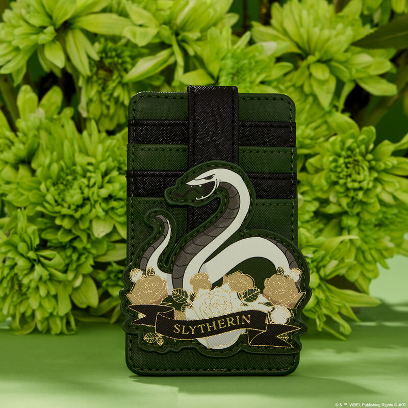 Green and black Slytherin card holder that has an appliqué of a grey and white snake on the front, sitting on top of white and pale gold flowers, sitting against a green background in front of a real bouquet of green flowers 